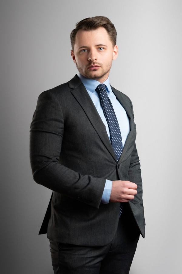 Portret biznesowy: mężczyzna w ciemnym garniturze na szarym tle